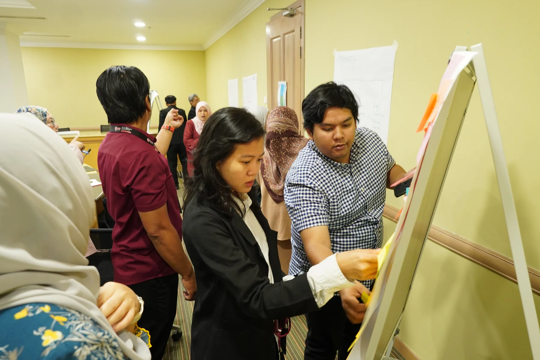 Izzati Azryna and Megat adding ideas to a workshop board with other stakeholders